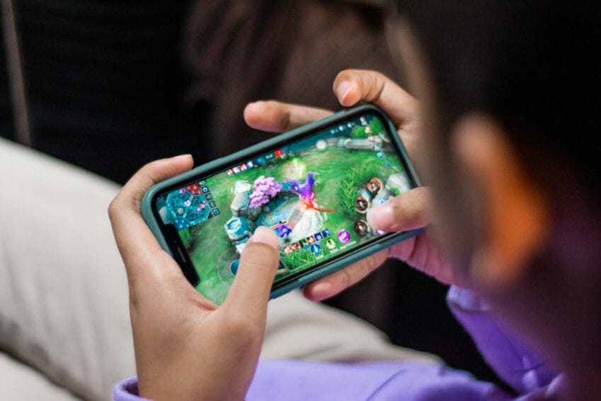 Hands holding a smartphone while playing a mobile game, illustrating the decision to top up in-game currency like Mobile Legends diamonds in the Philippines