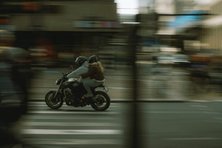 Motorcycle rider and helmeted passenger riding through Metro Manila traffic, representing an Angkas or JoyRide motorcycle taxi trip in the Philippines