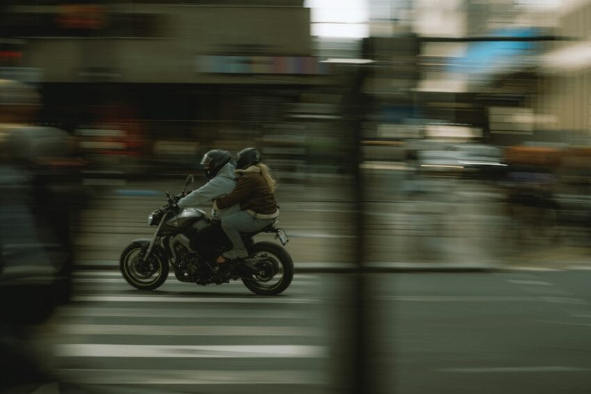 Motorcycle rider and helmeted passenger riding through Metro Manila traffic, representing an Angkas or JoyRide motorcycle taxi trip in the Philippines