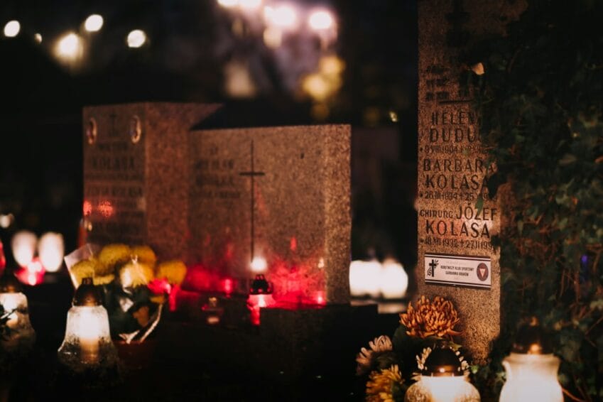 Grave markers covered with lit candles and flower offerings at night, the Filipino Undas tradition of visiting loved ones' graves for All Saints' and All Souls' Day